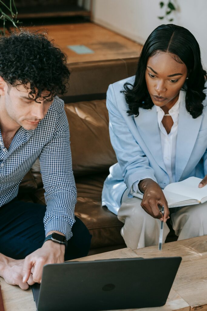 Two professionals working together closely on a laptop in a collaborative office setting.